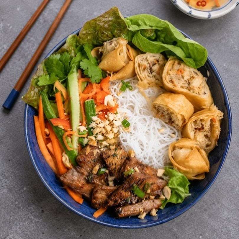 A vibrant Vietnamese vermicelli noodle bowl with grilled pork, spring rolls, and fresh vegetables.